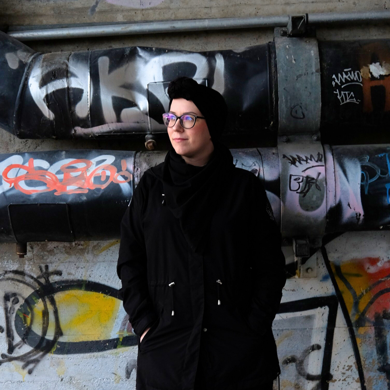 Nainen seisoo alikulkutunnelissa, jonka seinään on maalattu graffiteja.